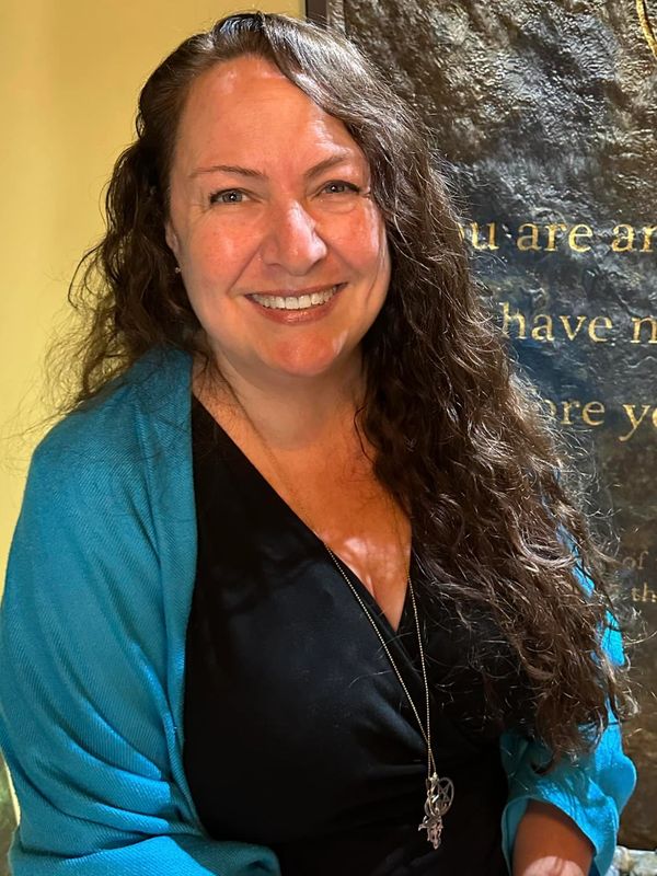 Smiling woman with long curly hair wearing a black top and blue shawl.