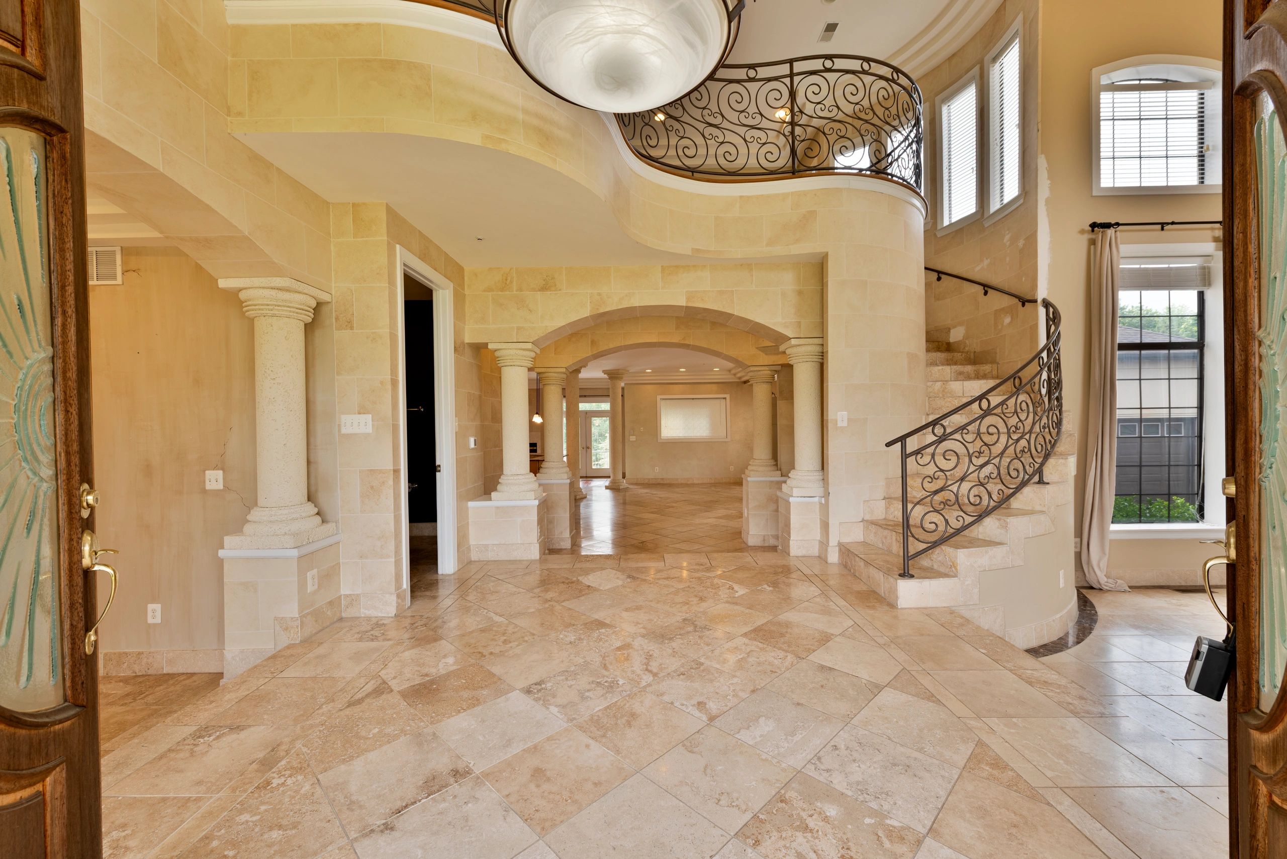 Elegant foyer with stone columns, arches, and a curved staircase with ornate railing.
