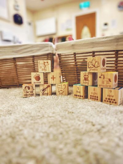 Wooden blocks with letters, numbers, and images stacked on carpet in front of wicker baskets.