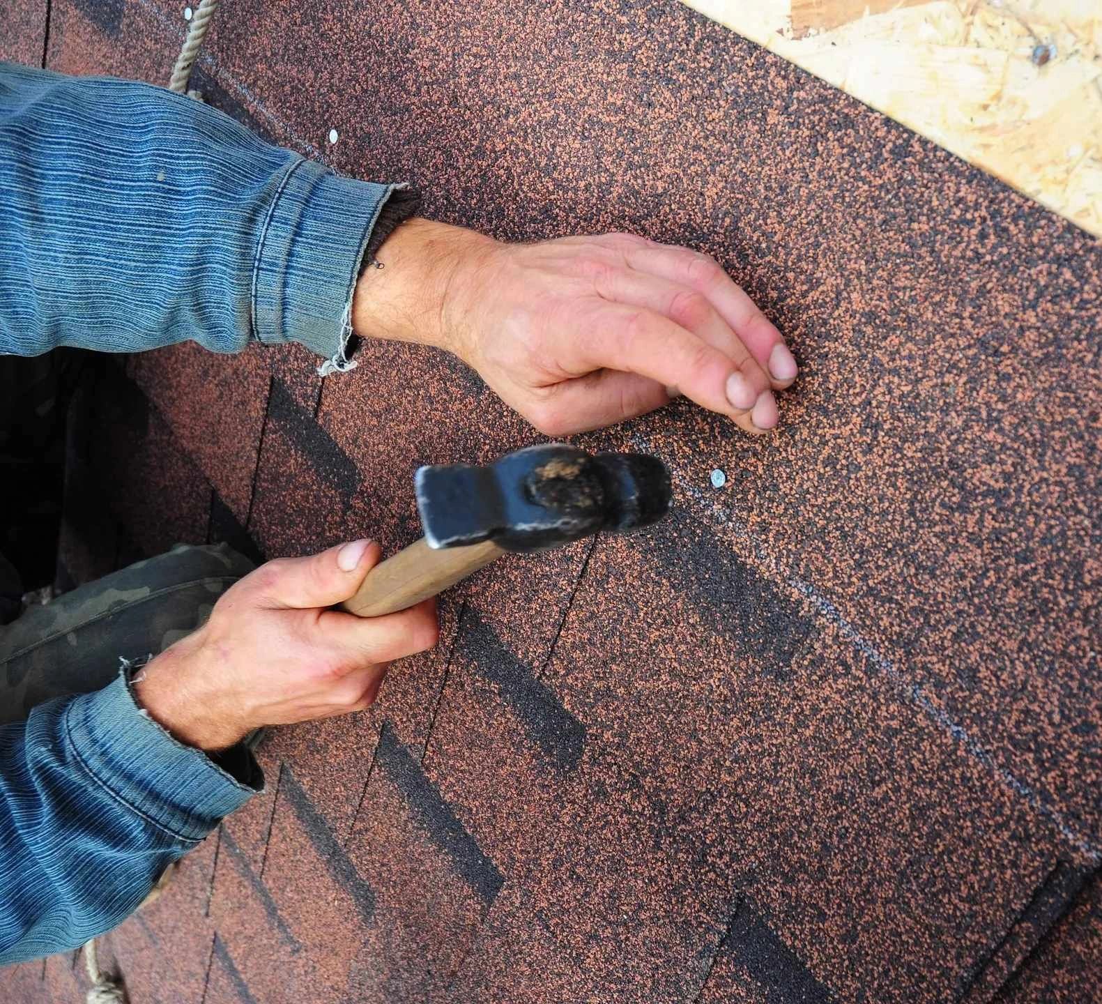 a man installing a shingle roof with a hammer