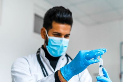 Doctor wearing mask and gloves preparing a syringe for injection.