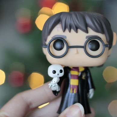 Close-up of a Harry Potter Funko Pop figure holding a tiny owl with blurred lights in the background.