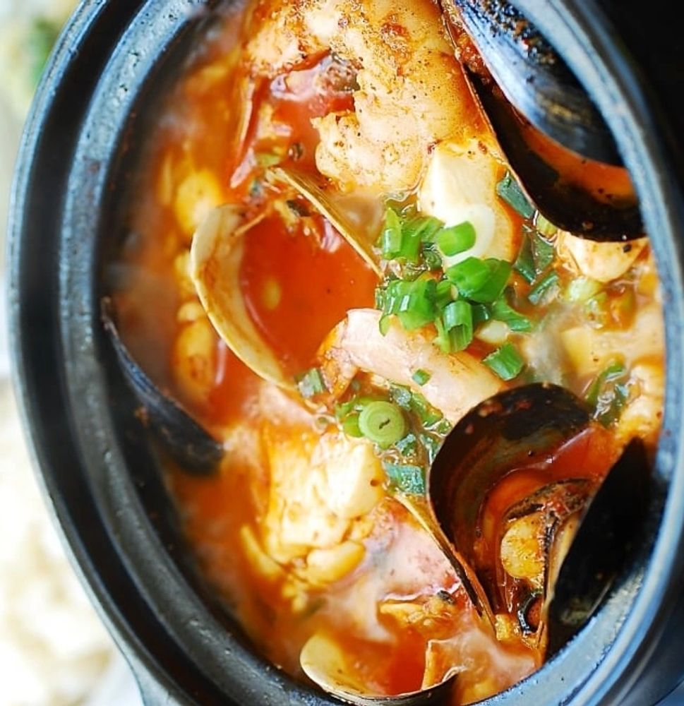 Spicy seafood stew with shrimp, mussels, and green onions in a black pot.