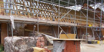 Building site with piles of bricks, scaffolding and exposed eaves. 
