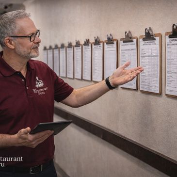Man in restaurant uniform reviewing multiple clipboards on a wall.