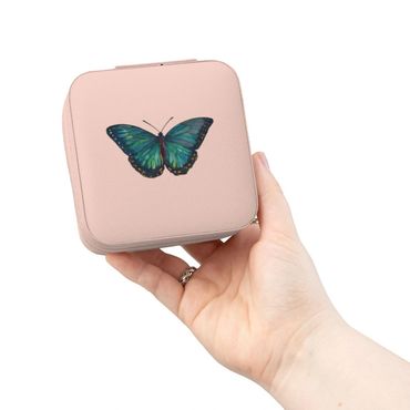 Hand holding a pink square box with a blue butterfly design.