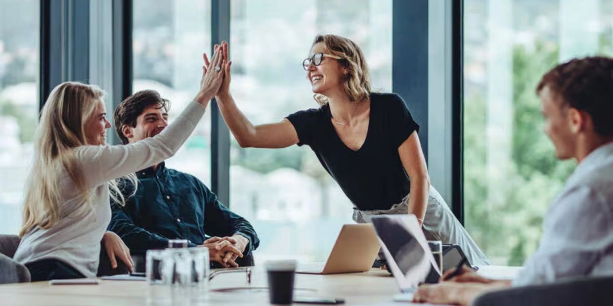 Colleagues sharing a high-five in a bright office meeting room.