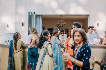 Guests in traditional attire socializing near an outdoor bar at a festive event.