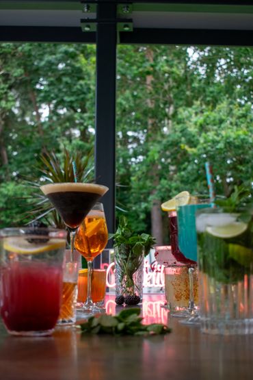 Colorful cocktails and fresh mint on a bar table with greenery outside.