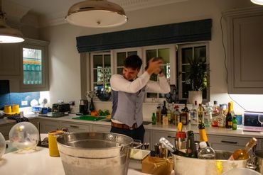 A man joyfully shaking a cocktail shaker in a home bar setup.