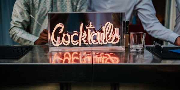 Neon sign reading 'Cocktails' on a bar counter with people in the background.