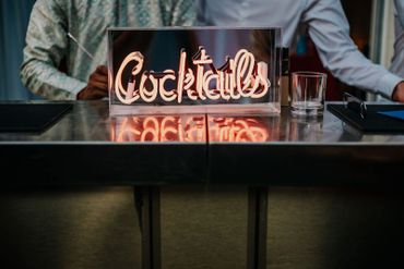 Neon sign reading 'Cocktails' on a bar counter with people in the background.