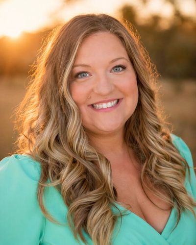 Smiling woman with long curly hair in a turquoise dress at sunset.