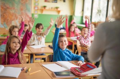 Happy students eagerly raising hands in classroom.