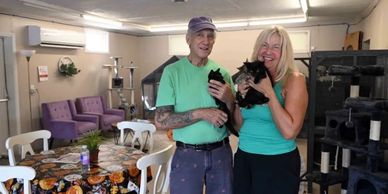 Two people happily holding black kittens in a cozy room with cat furniture.