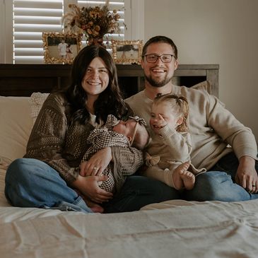Happy family sitting on a bed with two young children.