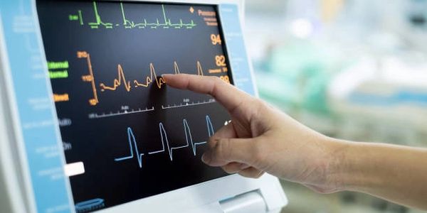 Hand pointing to vital signs on a medical monitor screen.