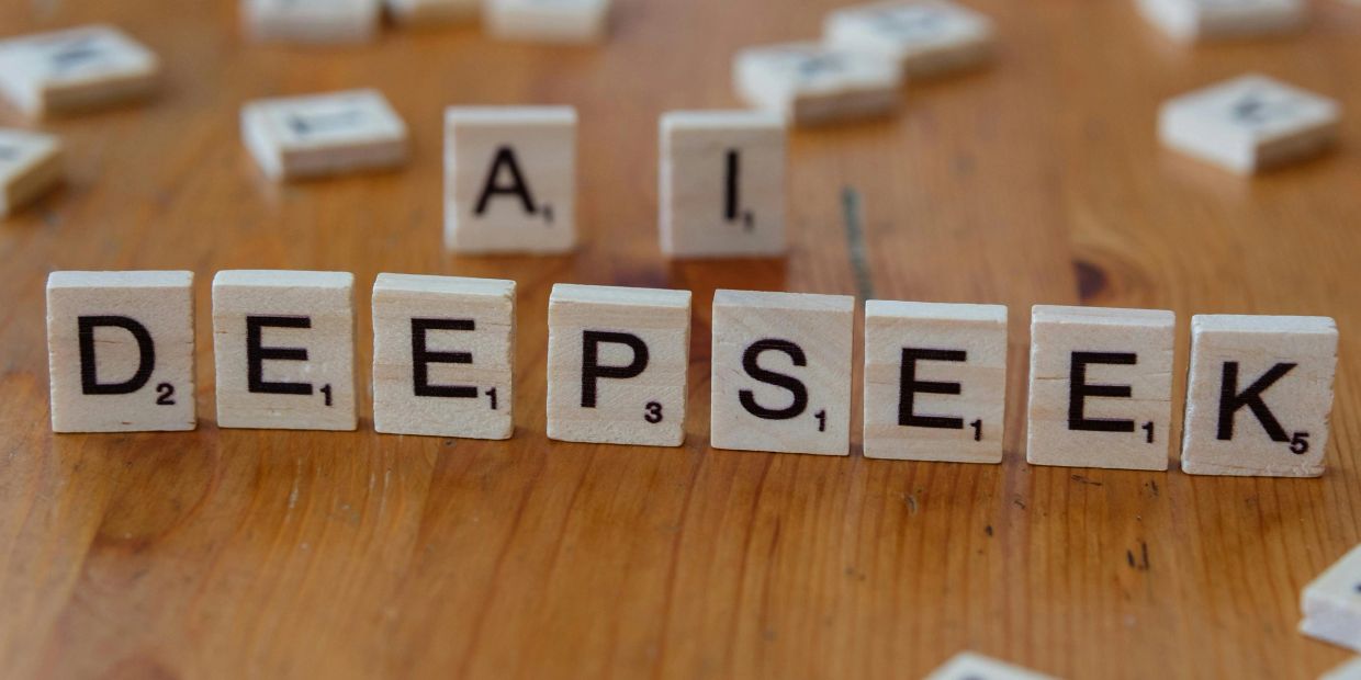 Scrabble tiles spell out 'DEEPSEEK' on a wooden surface.
