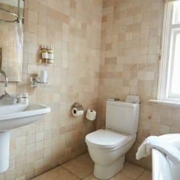 Bright bathroom with tiled walls, a pedestal sink, toilet, and bathtub.
