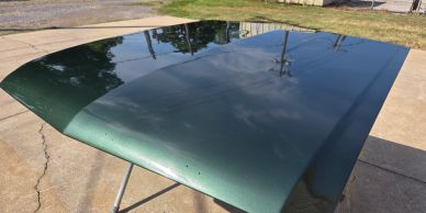 Green metal car hood reflecting the sky.