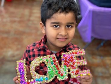 A boy holding a colorful 'LOVE' sign with decorative beads.