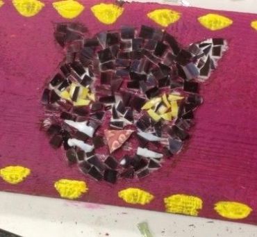 Mosaic artwork of a cat's face on a purple background with yellow accents.