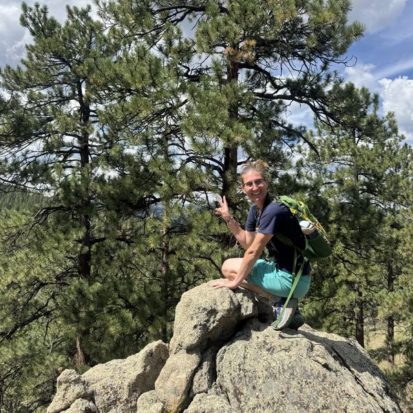 Person posing on a rock with peace sign in a forested area.