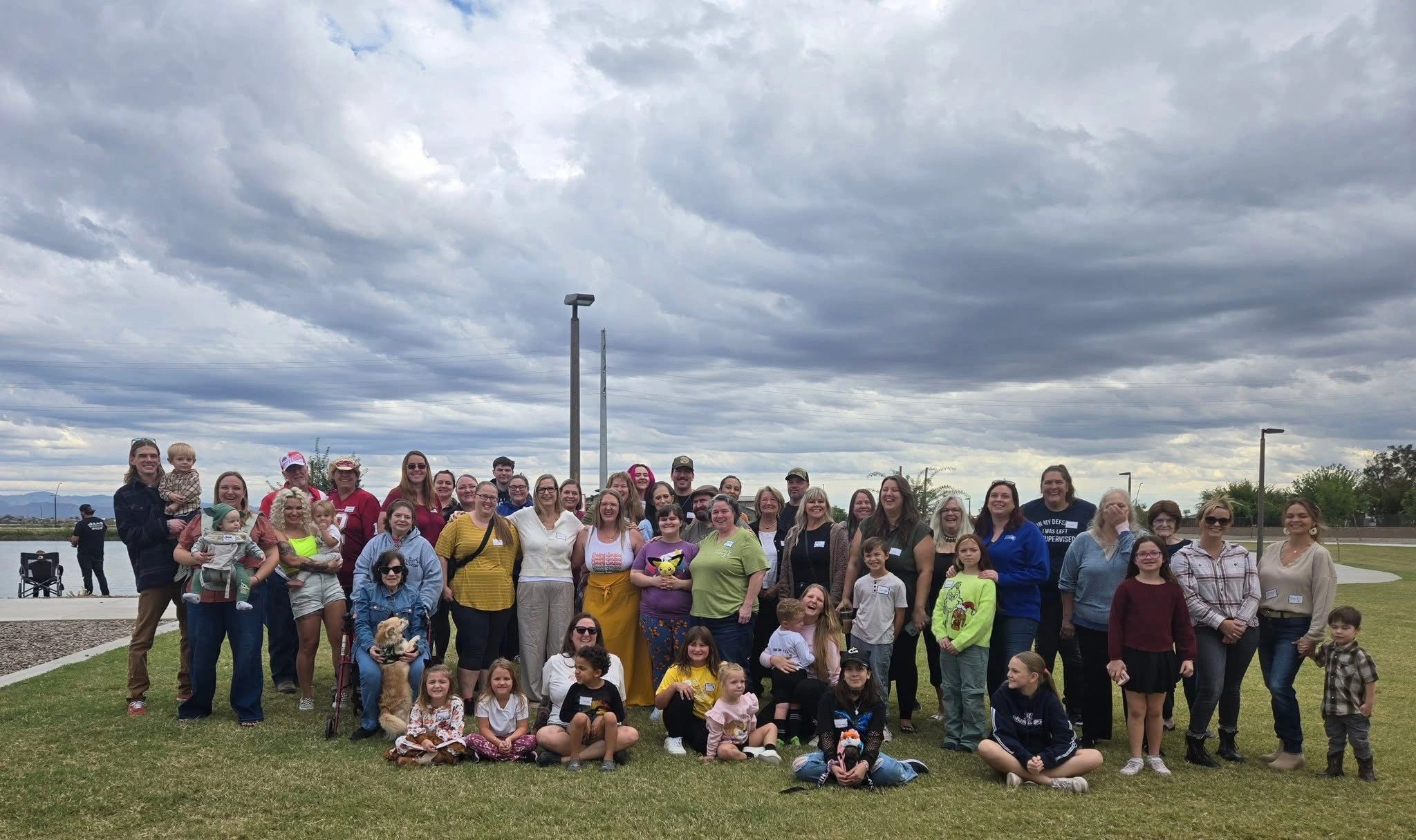 Large group of people posing outdoors under cloudy sky.