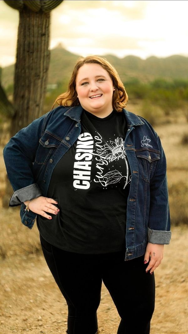 Woman in denim jacket and black shirt smiling outdoors with desert background.