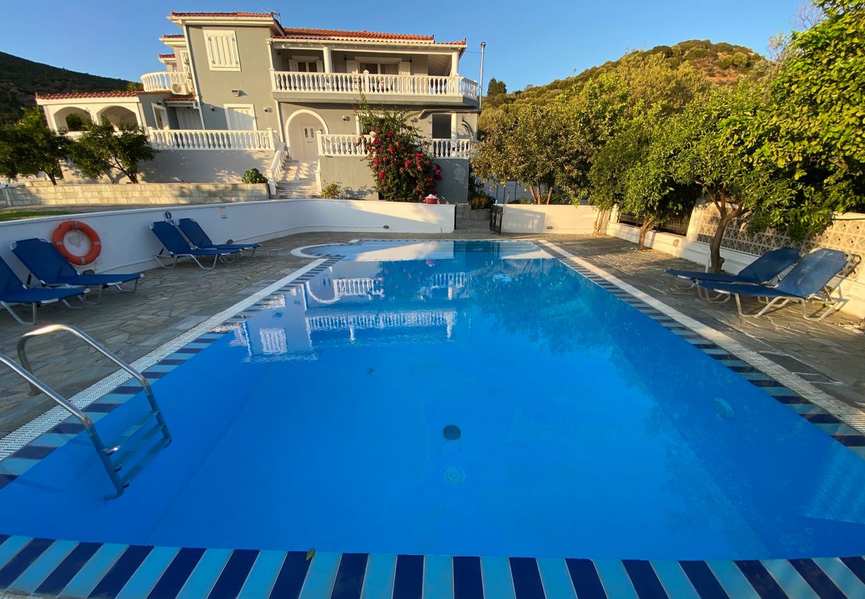 A serene swimming pool with lounge chairs beside a large house on a sunny day.