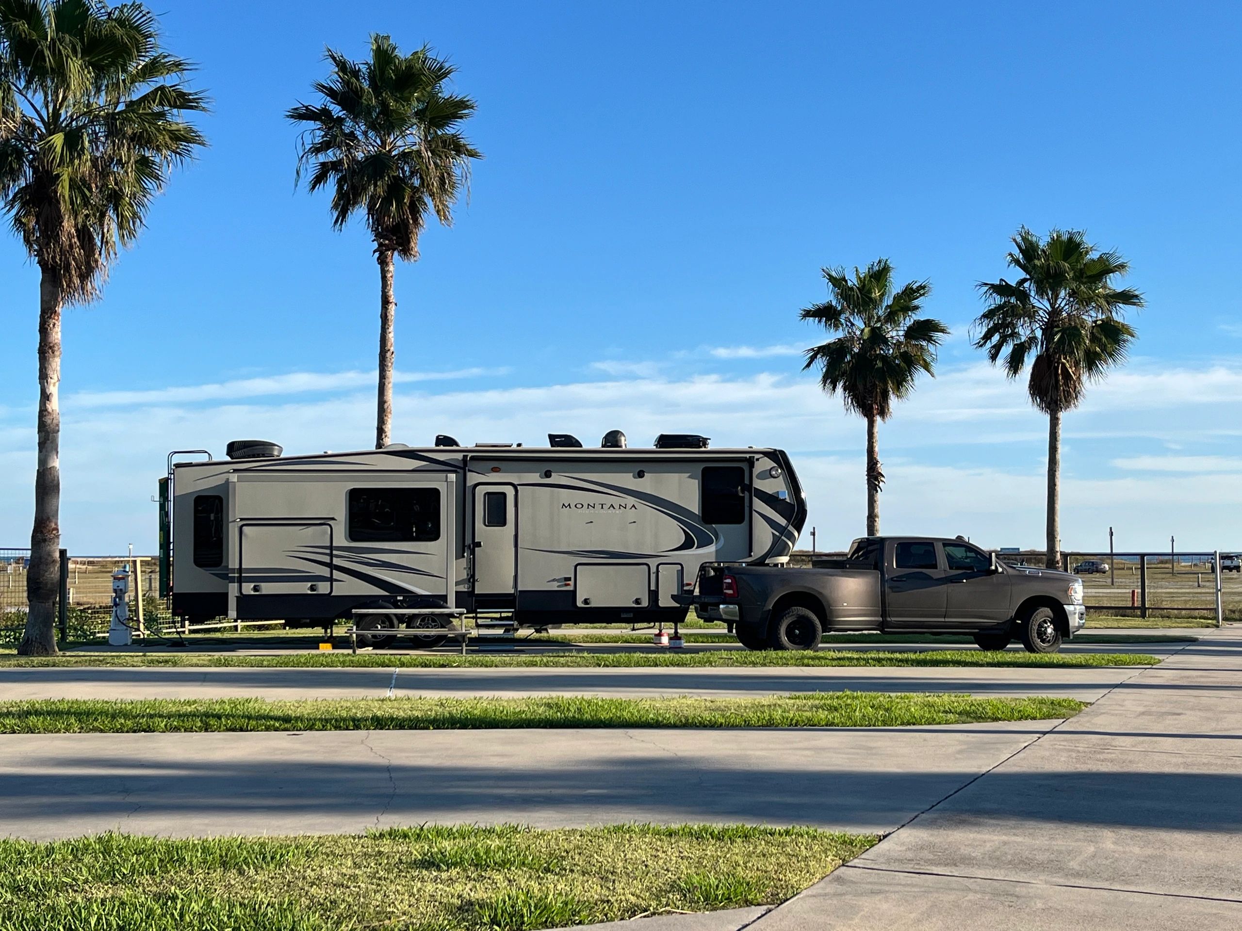 RV trailer hitched to a pickup truck next to palm trees.