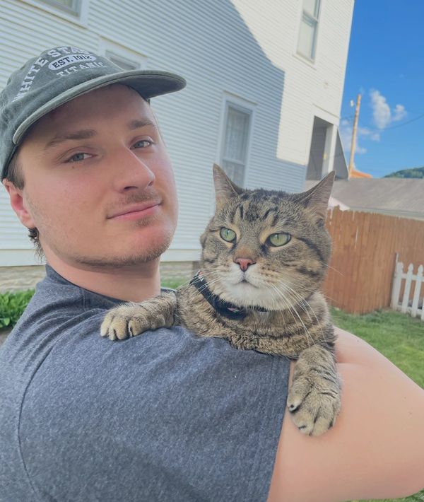 A man holding a tabby cat outdoors near a house.