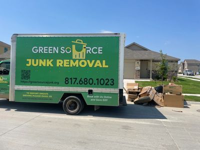 Green Source Junk Removal Truck next to a pile of cardboard boxes in the curb. 