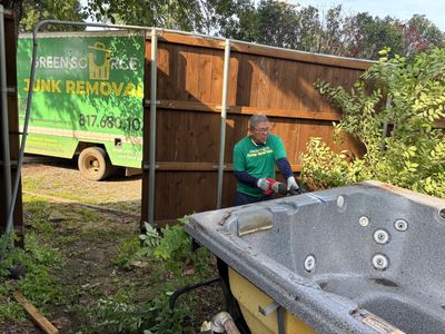 Green Source Junk Removal employee cutting down hot tub.