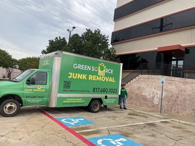 Green Source Junk Removal truck parked in handicapped spot beside building.