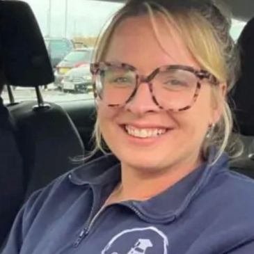 A smiling woman with glasses sitting in a car.