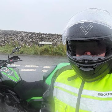 Person in motorcycle gear with bike and road sign.