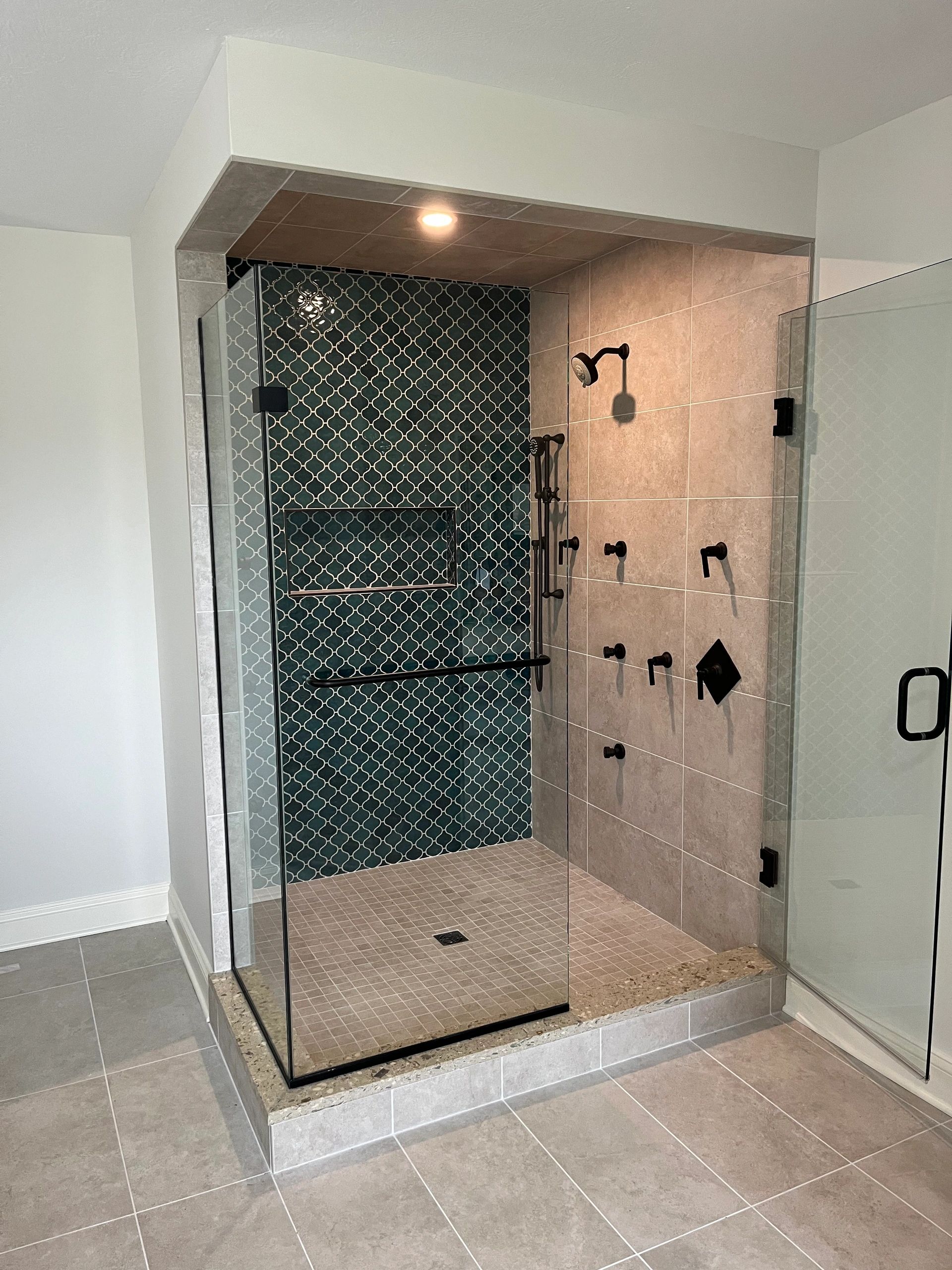 Modern tiled shower with glass enclosure and black fixtures.