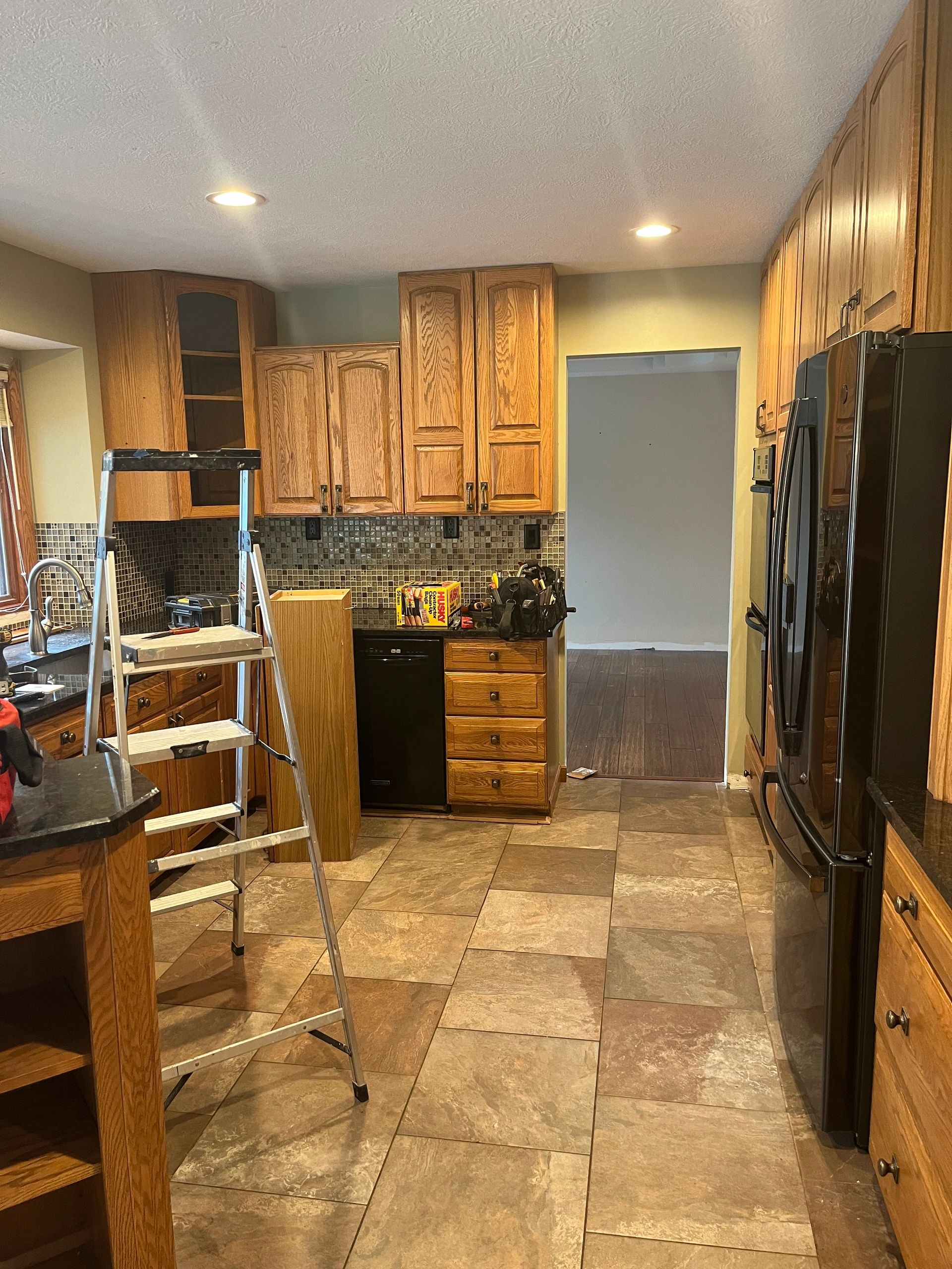 Kitchen with wooden cabinets, tiled floor, and a ladder for renovation.