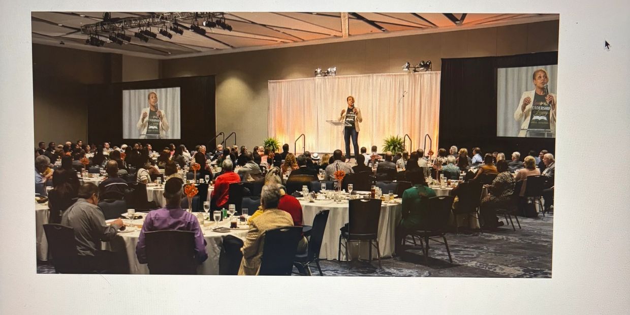 Speaker addressing a large audience at a formal event in a banquet hall.