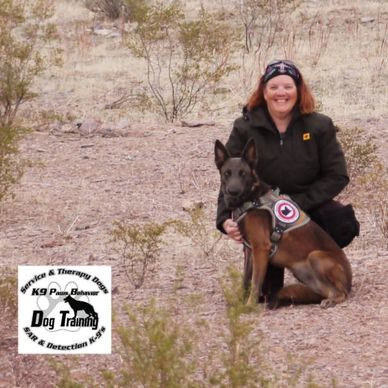 Woman kneels beside a service dog in a desert landscape.