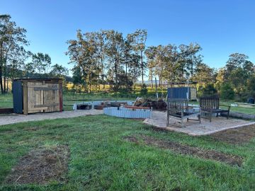 Rustic outdoor firepit area with wooden chairs and a shed.