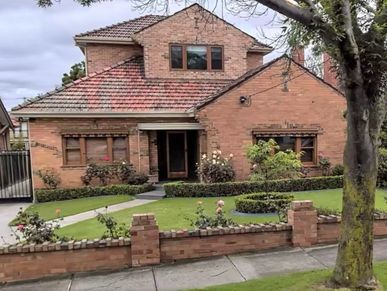 A brick house with a neat garden and a tree in front.