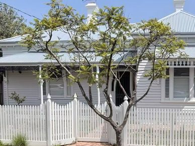 Charming white house with a picket fence and a leafy tree in front.