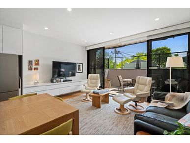 Modern living room with white armchairs, leather sofa, and outdoor patio seating.