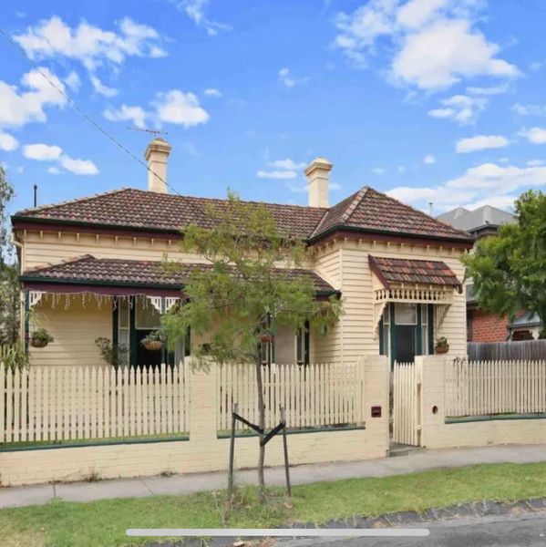A charming beige house with a tiled roof and a picket fence under a bright blue sky.