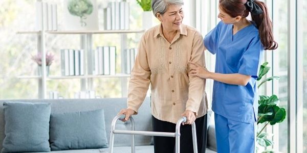 Nurse assisting elderly woman with walker indoors.