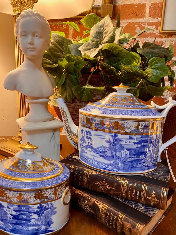 Elegant vintage scene with porcelain teapot, bust sculpture, and classic books.
