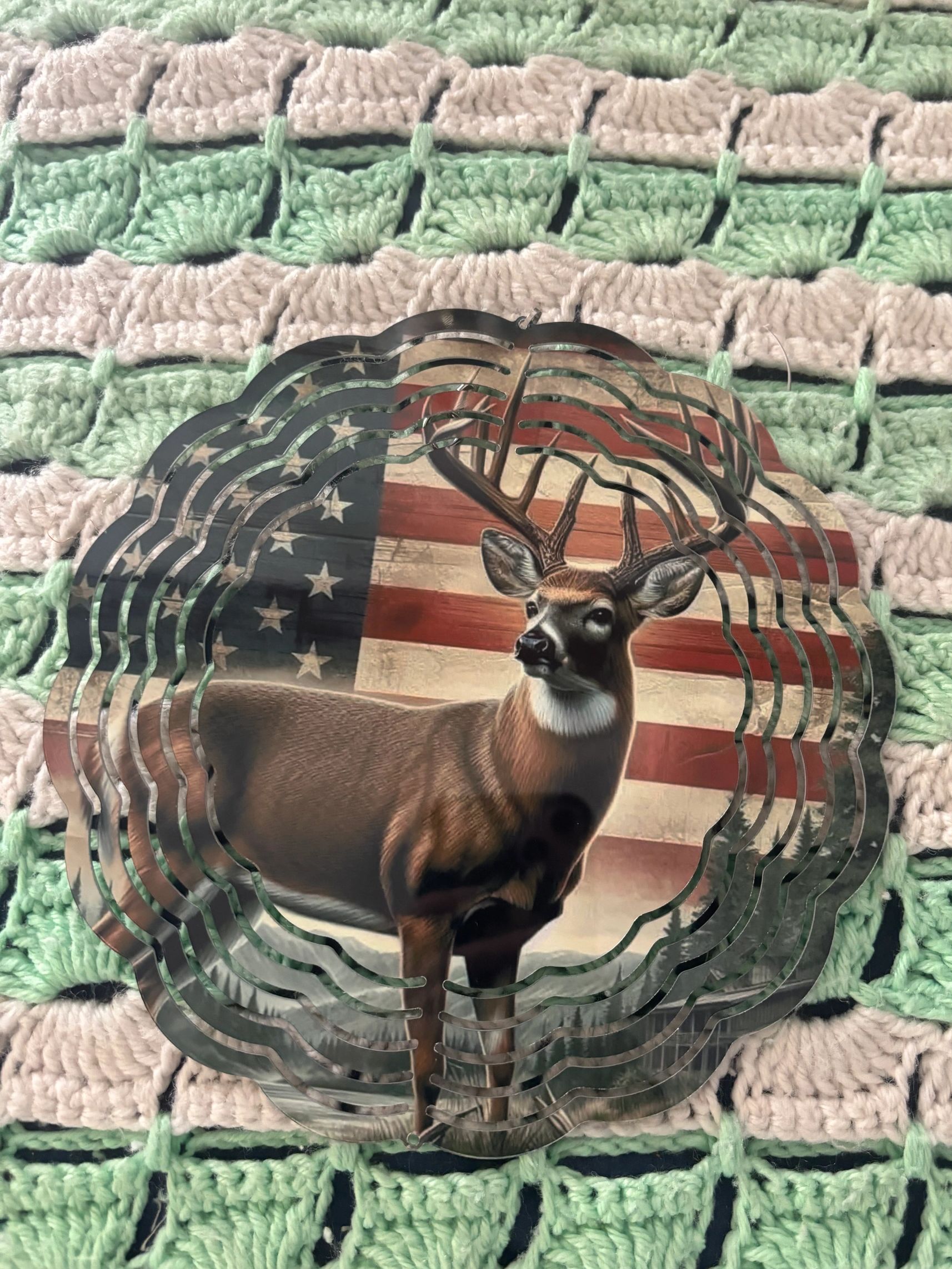Metal deer silhouette with American flag background on a crocheted blanket.