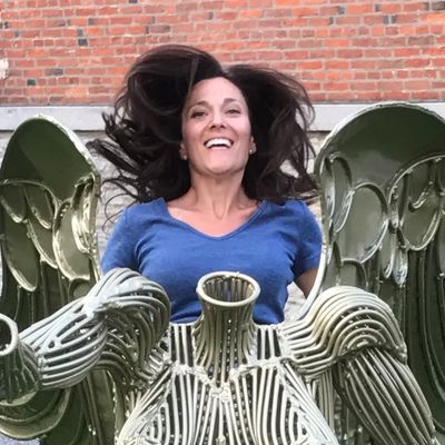 Woman jumping in the air behind a bronze statue of a woman with wings.